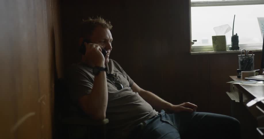 A man talks on a phone while sitting at a desk