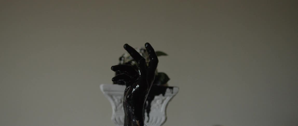 A hand covered in black ink opens its fist in front of a pedestal