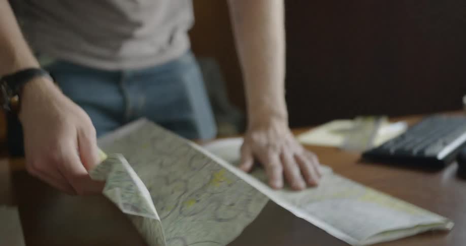 A man unfolds a map and lays it on a desk