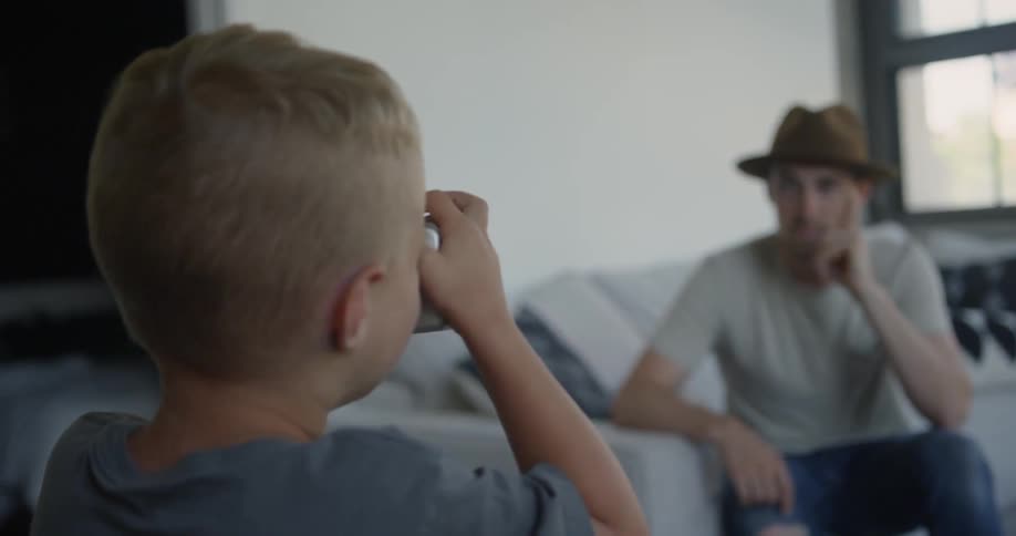 A man sits on a sofa and poses as a young boy takes his photo with a camera