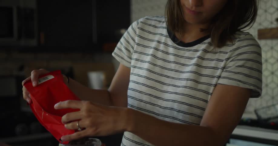 A woman stands in a kitchen and pours coffee beans into a glass jar