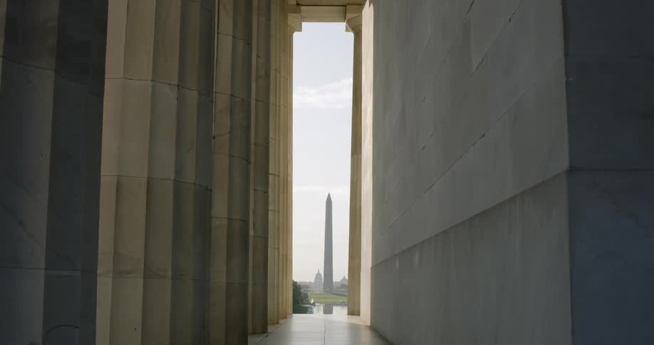 The washington monument stands in the distance from pillars of the Lincoln Memorial