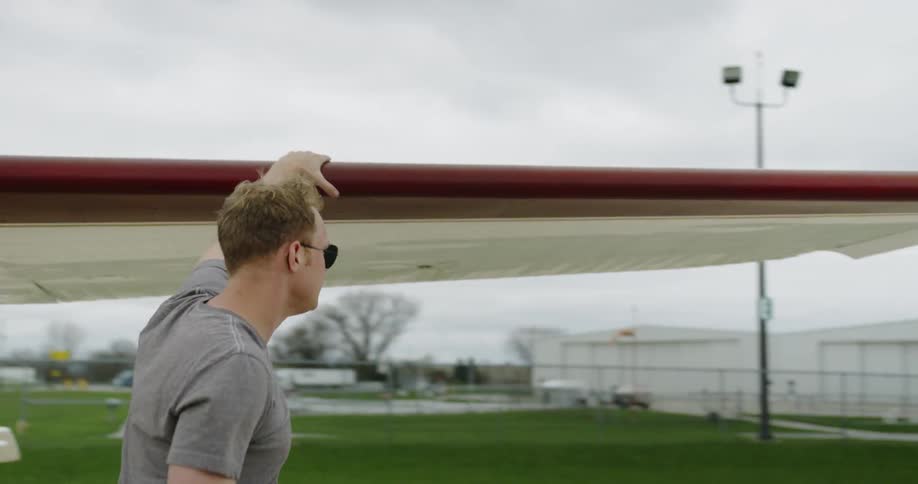 A man rubs his hand along the wing of a small aircraft