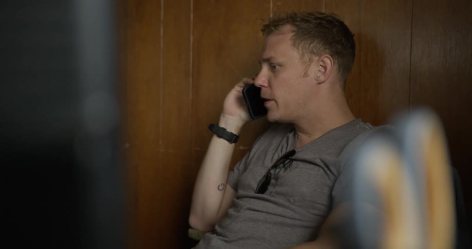 A man talks on a phone while sitting at a desk