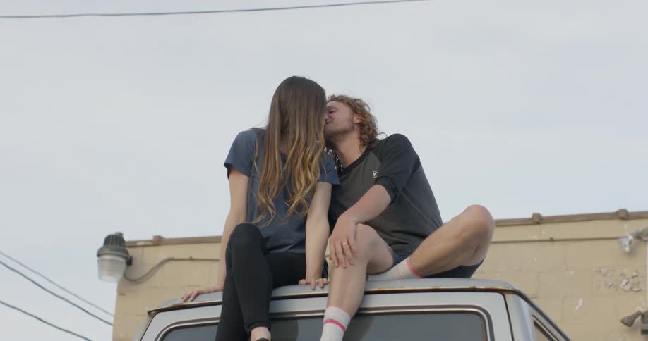 A man and woman kiss while sitting on a car roof