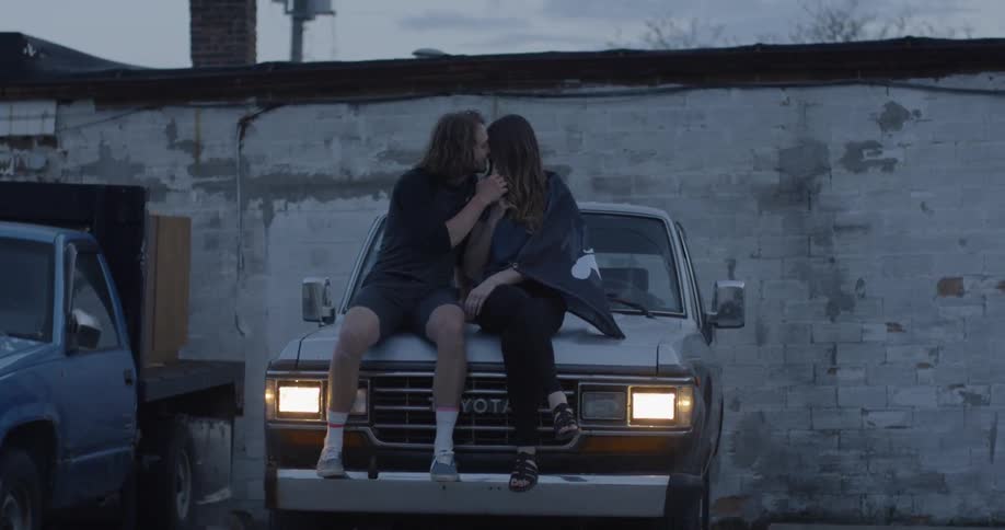 A man and woman kiss on the hood of a truck