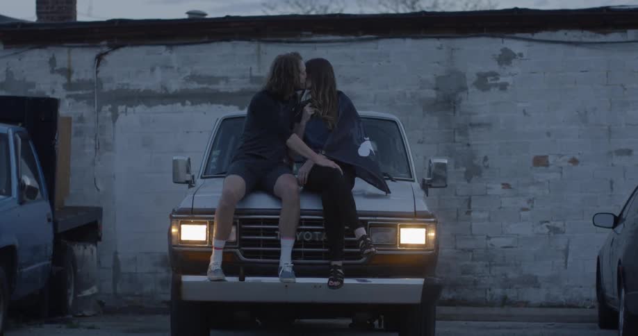 A man and woman kiss on the hood of a truck