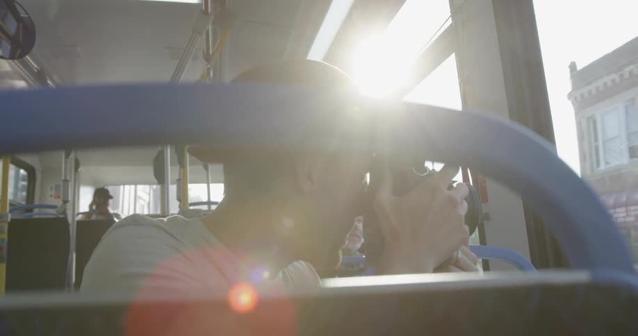 Man rides on a bus looking out the window and taking pictures