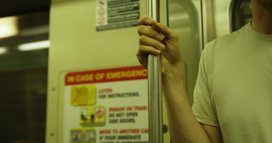 Man stands riding on a subway holding onto a pole