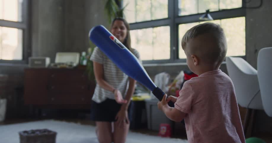 Woman tosses a ball and a child tries to hit it with a blue bat