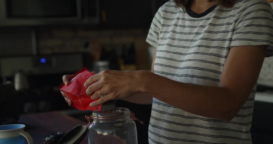 Woman pours coffee beans from a bag into a glass jar