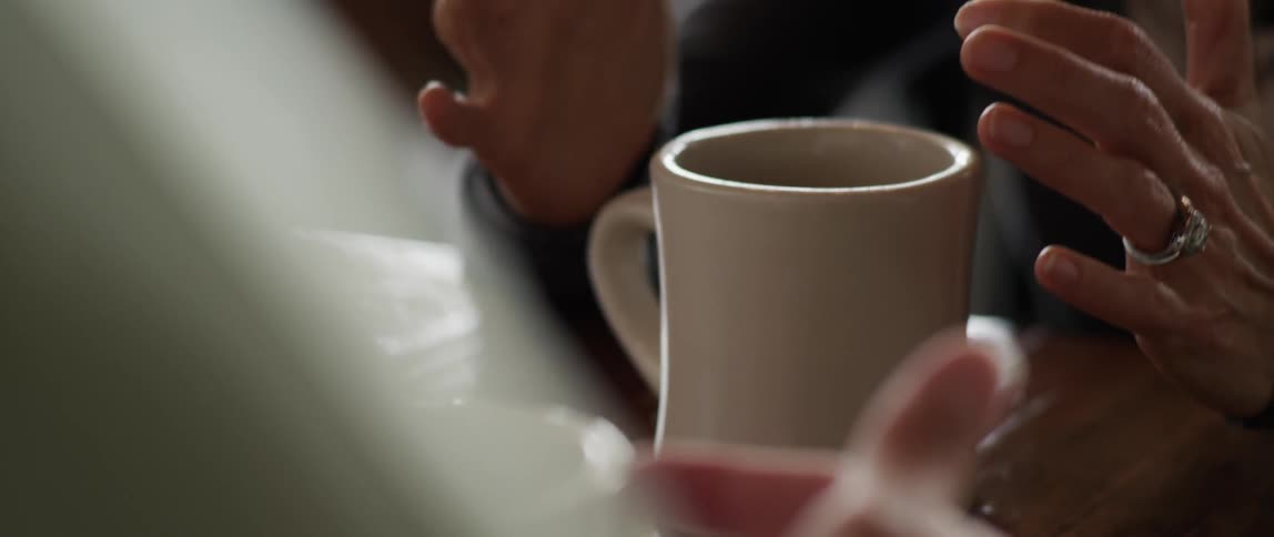 A woman touches the top of her mug and talks