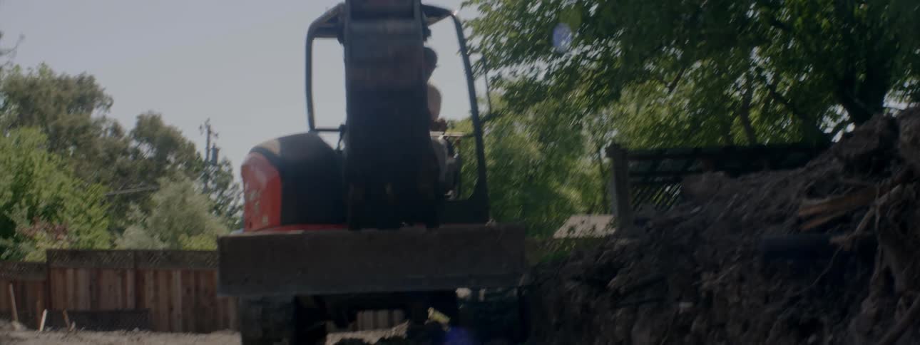 A man operates a construction vehicle to move dirt from a hole in the ground