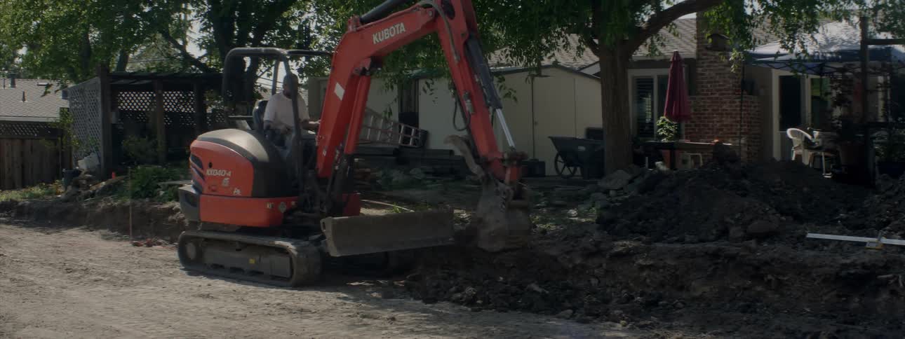 A man sits in a construction vehicle picking up rocks and dirt and moving them