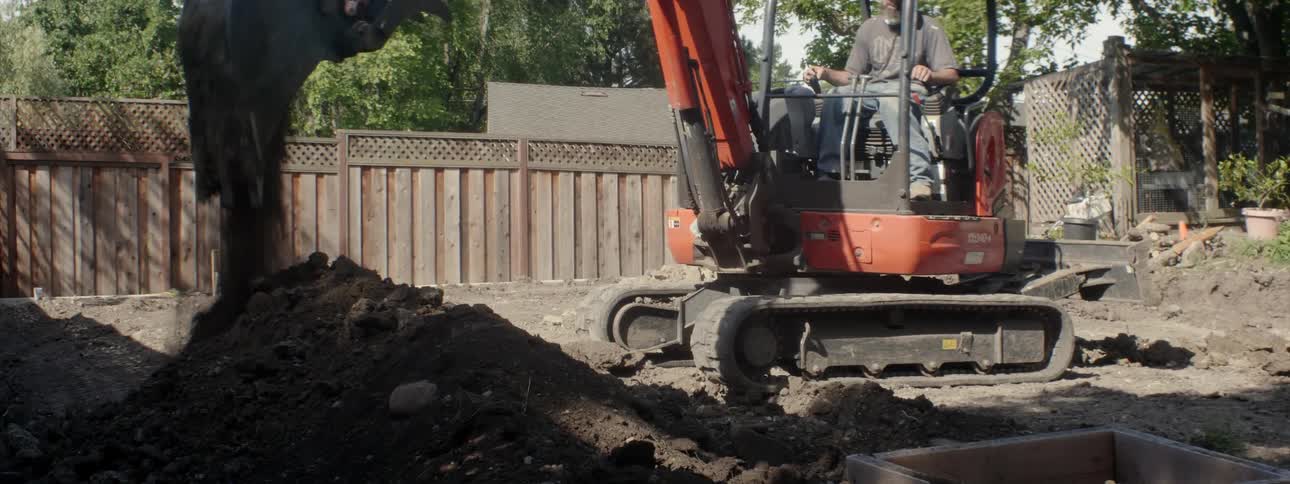 An excavator digs up dirt in a backyard