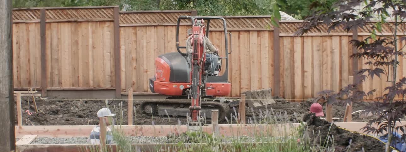 Man uses a backhoe to dig dirt and then dump it in another location