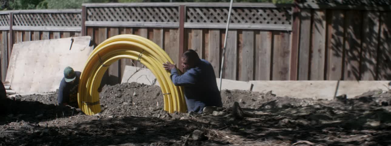 Two men push a spool of wire at a construction site