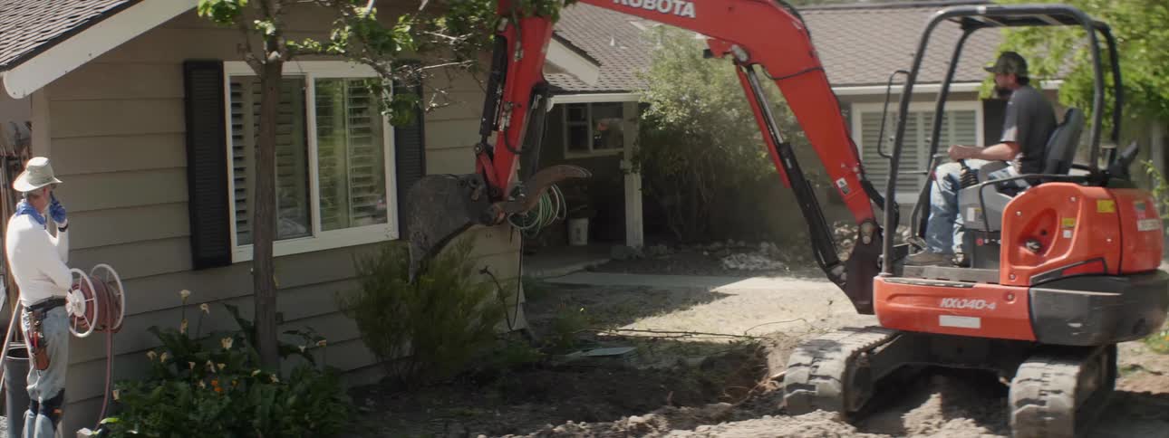 An excavator tears out plants at a house