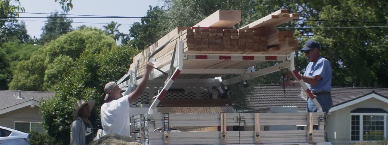 Construction workers unload wood from a truck