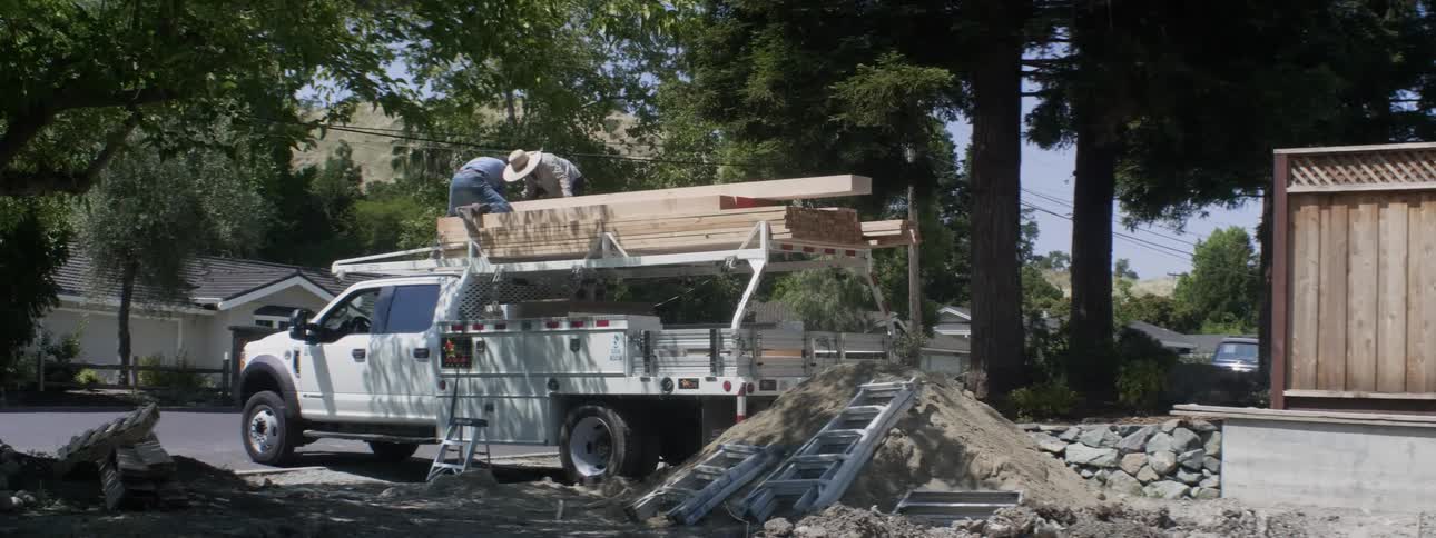Workers unload wood planks from a truck at a construction site