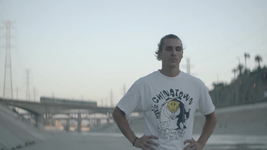 A man stands in front of a bridge with a train traveling on it at sunset