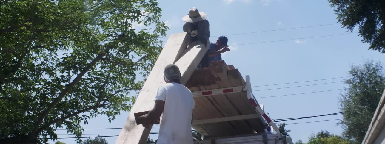The construction workers are handing down a huge piece of lumber