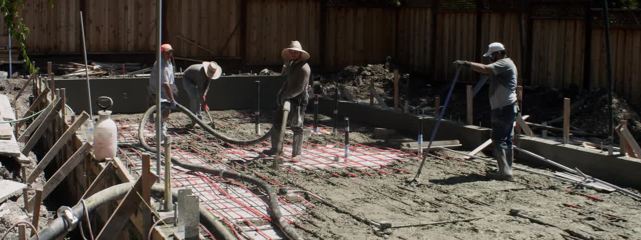 A group of workers laying cement with a hose at a construction site