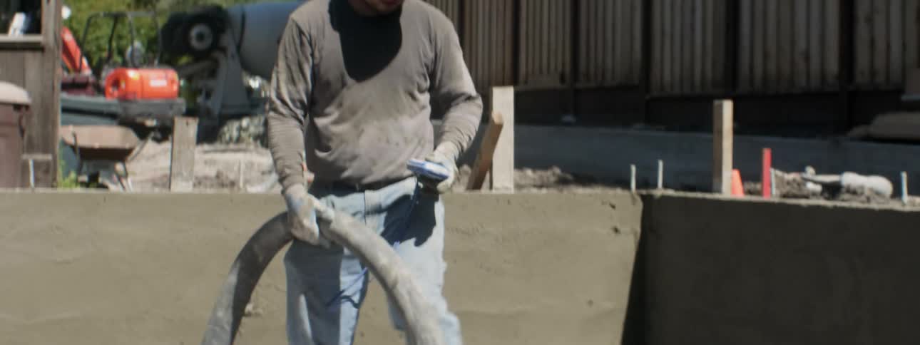 A workers lays concrete in a backyard
