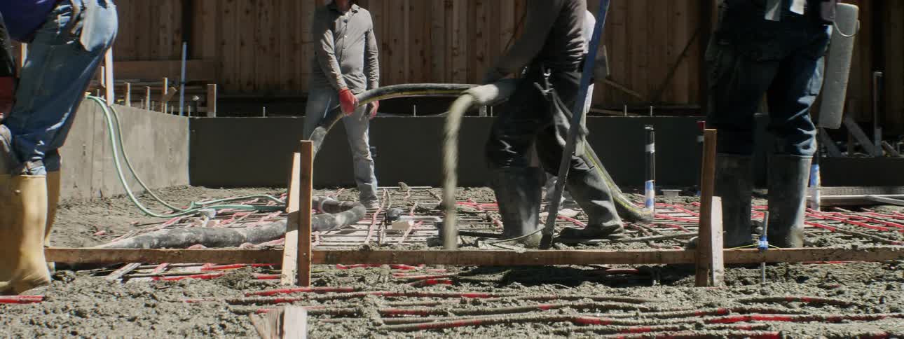 Men hold onto a hose as they spread cement into a foundation