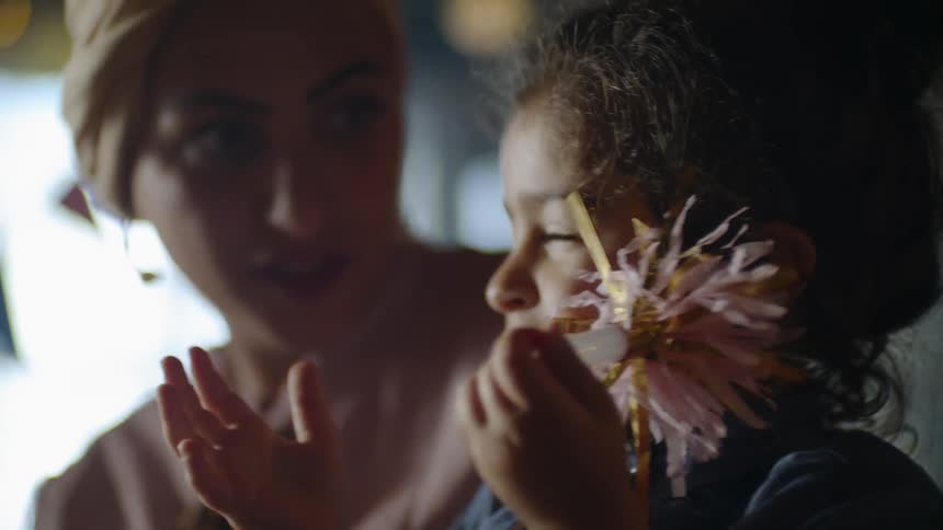 Woman is talking to little girl who is playing with party horn