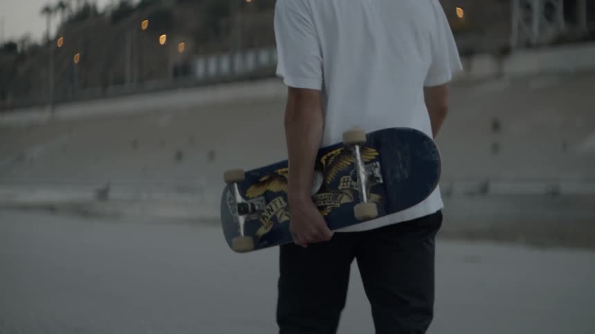 The man carries his skateboard at sunset