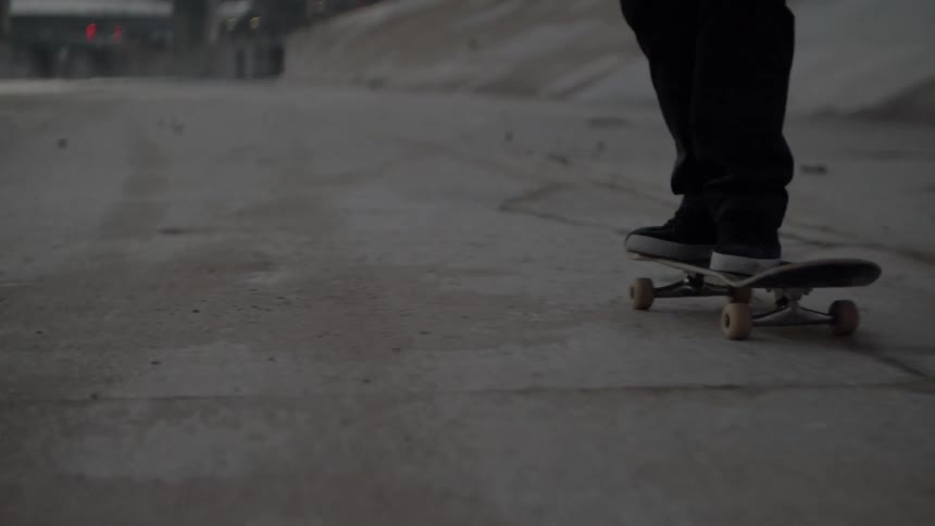 A skateboarder rides over concrete at sunset