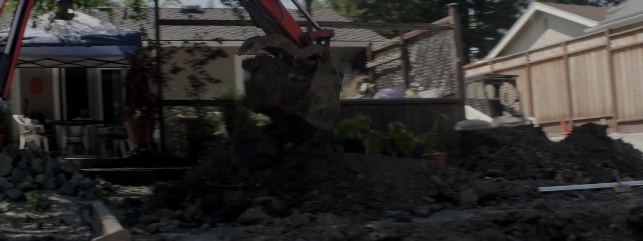 An excavator digs up dirt in a backyard