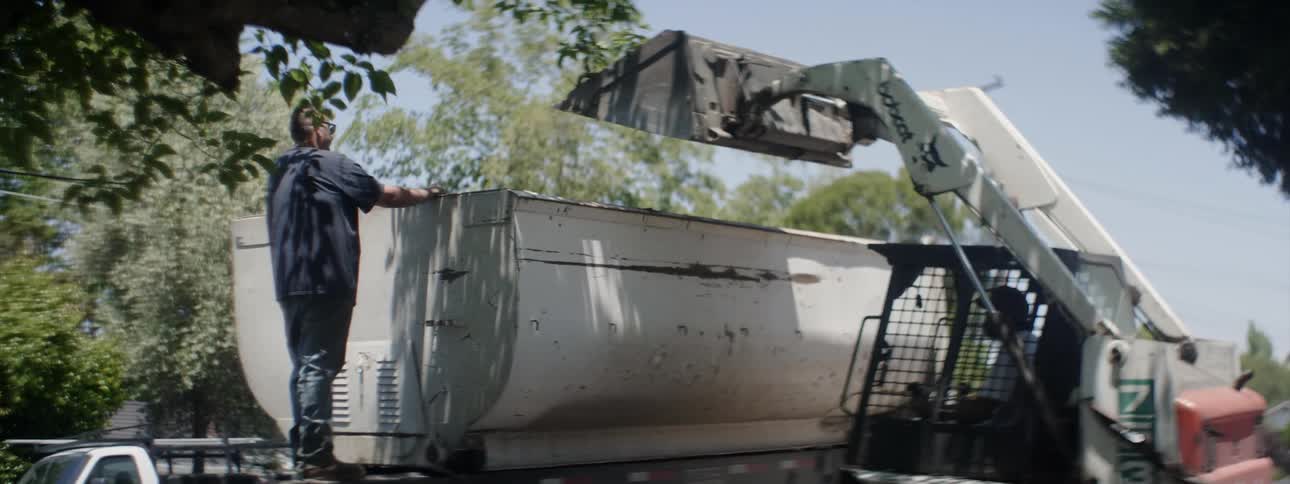 A man operates a bobcat vehicle to lift debris into a truck