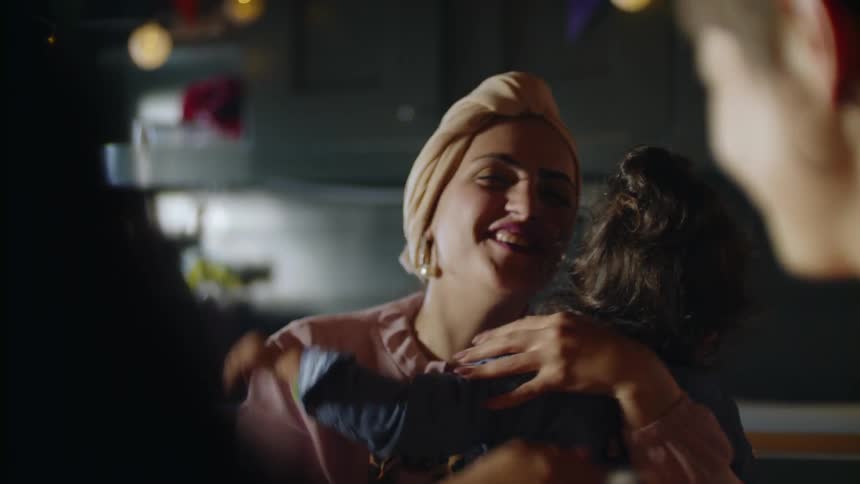 A woman sitting in a dining room with other women hugs and kisses a little girl