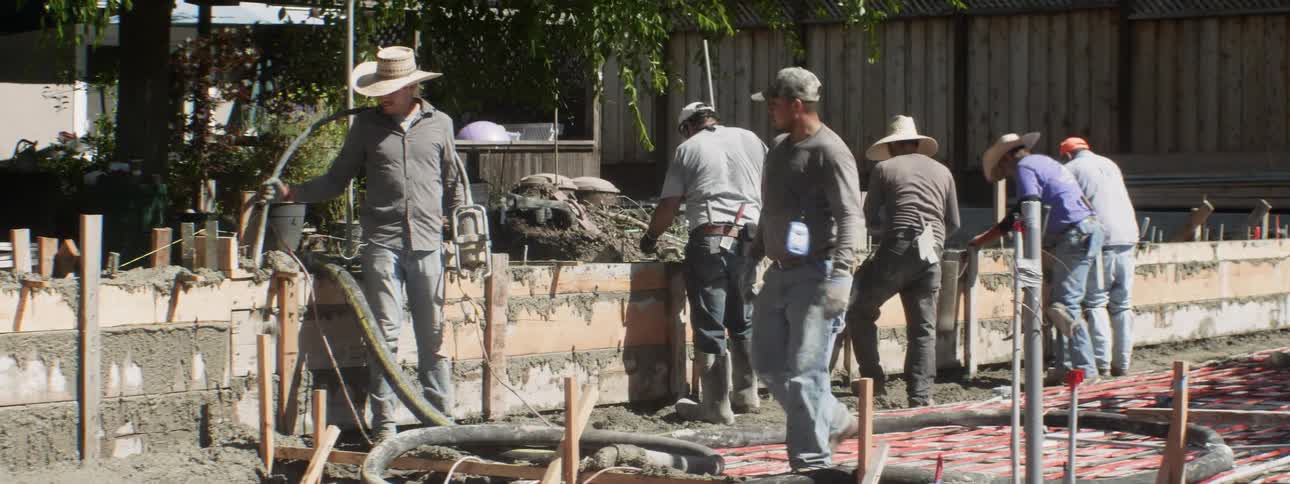 A group of construction workers laying cement and hammering wood at a construction site