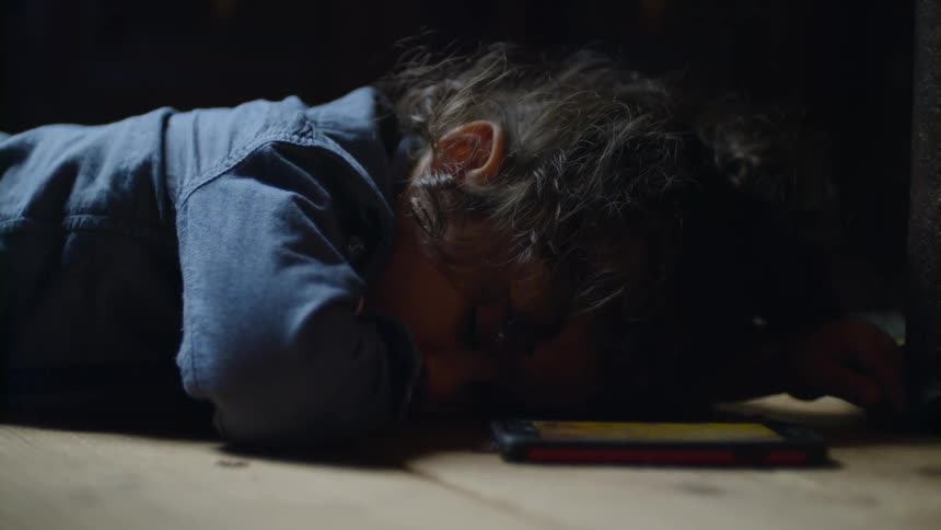 A little girl lays sleeping on the floor next to a cell phone