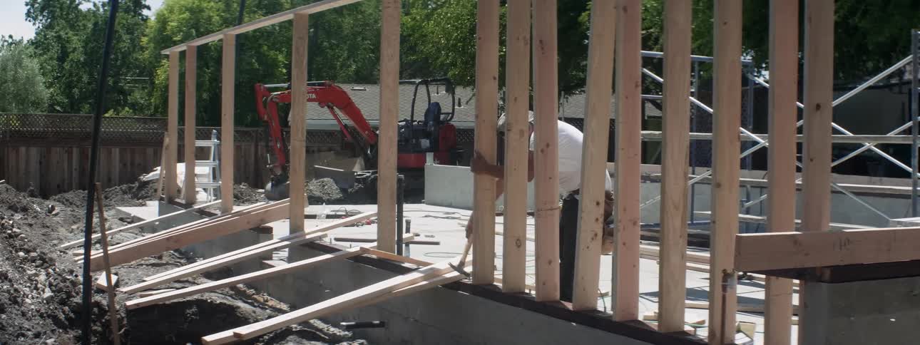 A man hammers nails into wood at a construction site on a sunny day
