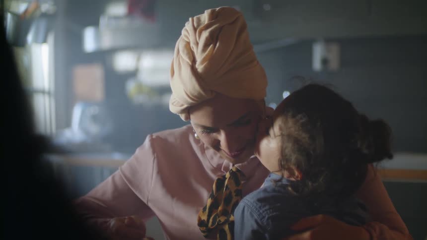 A little girl sits on a woman's lap and whispers in her hair