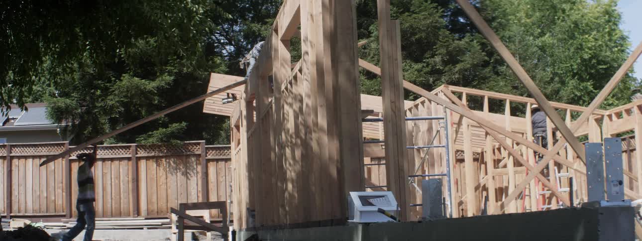 Construction workers add a large beam of wood to the frame of a building