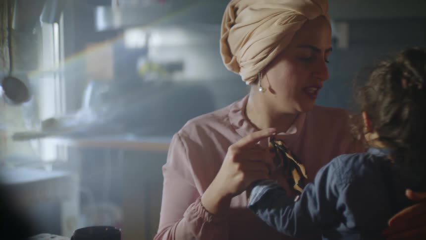 A woman smiles while rubbing frosting on a girl's nose
