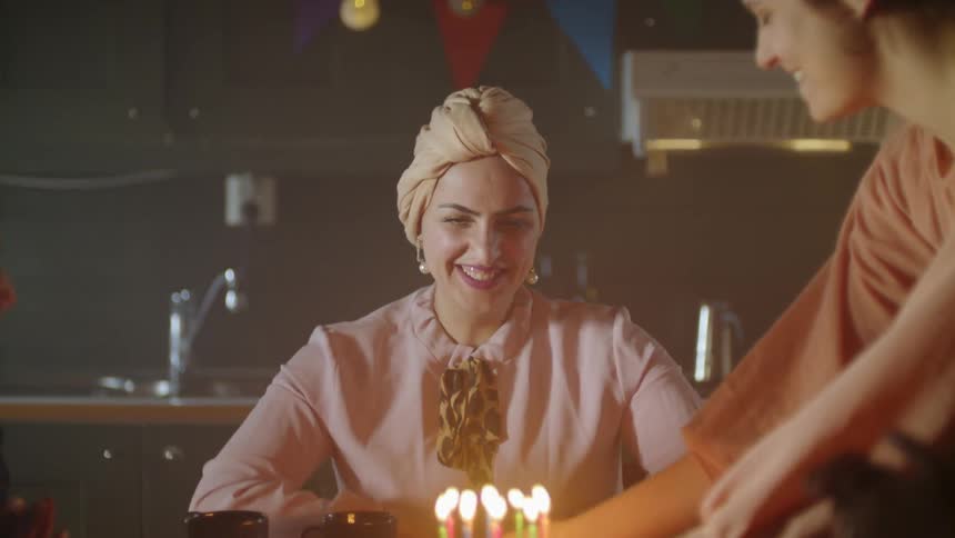The woman laughs as a birthday cake is brought in