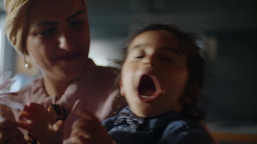 A little girl sits on a woman's lap and laughs as they play with a toy