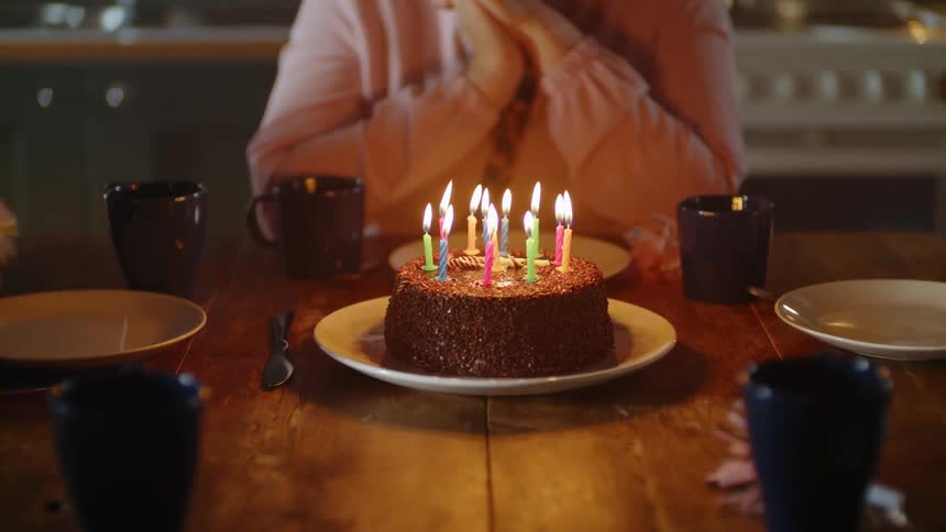 Woman blows out candles on top of birthday cake with friends