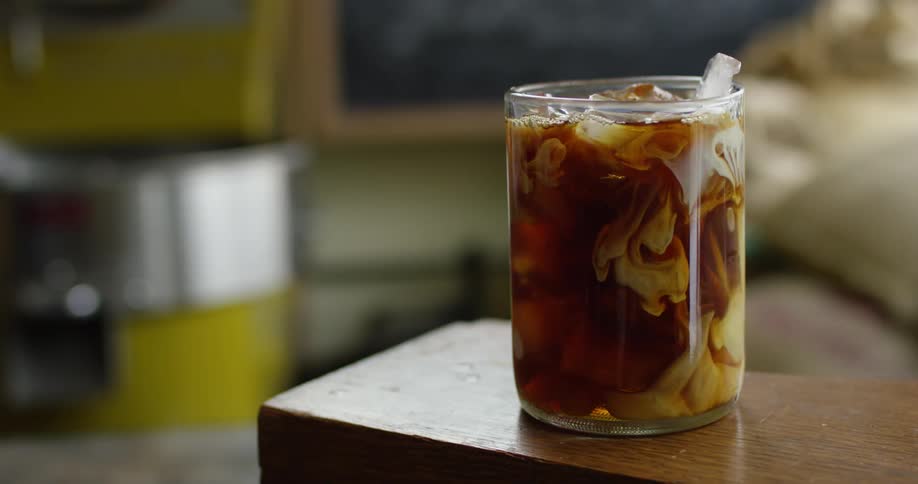 A glass filled with ice and a drink has cream poured over the top