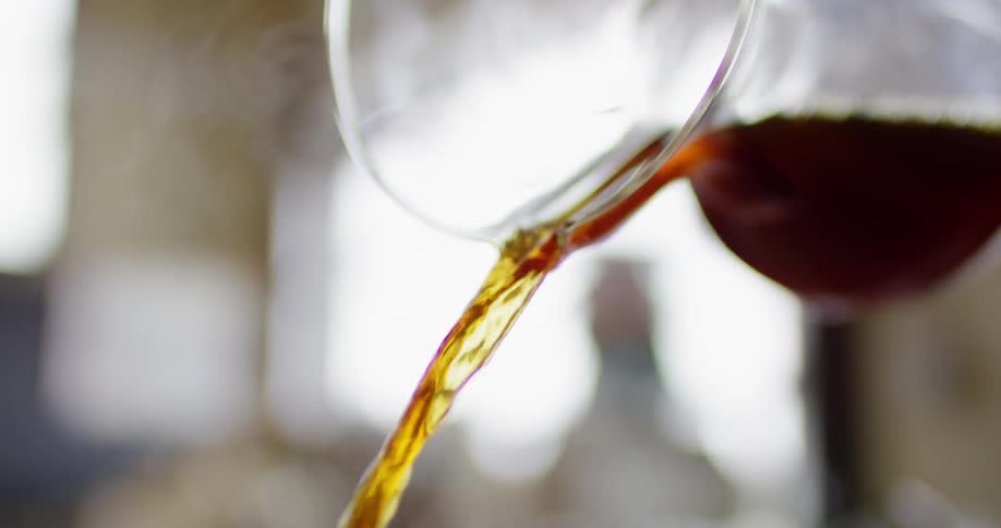A clear glass pitcher pours steaming brown liquid