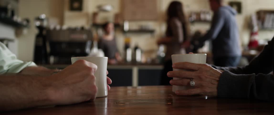 View of a coffee shop with two people sitting each holding mugs