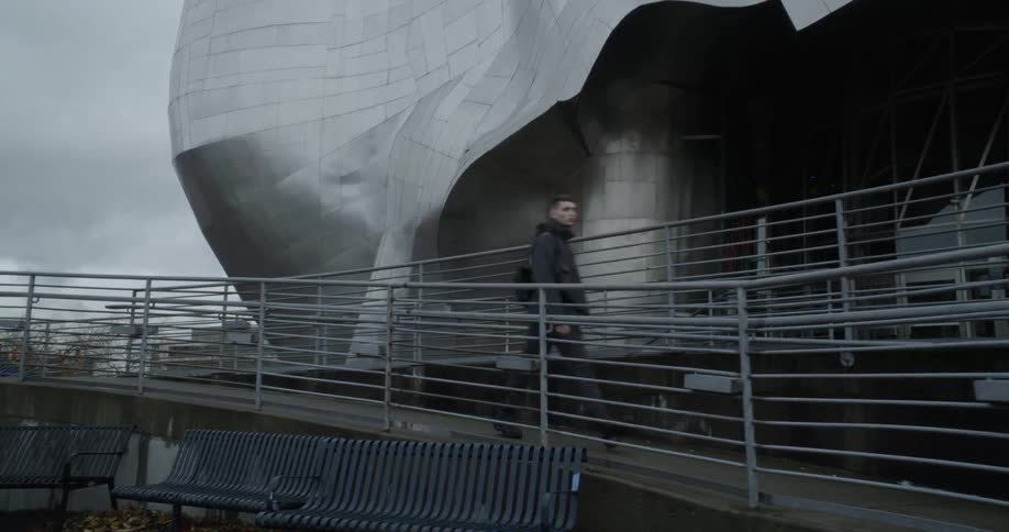 A man walks down a ramp outside of a building on a cloudy afternoon