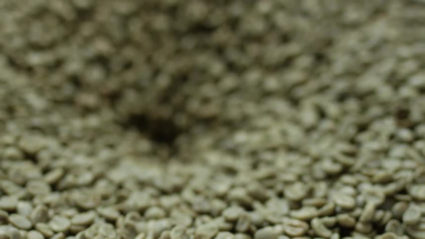 Green coffee beans flow down through a hole in a large vat