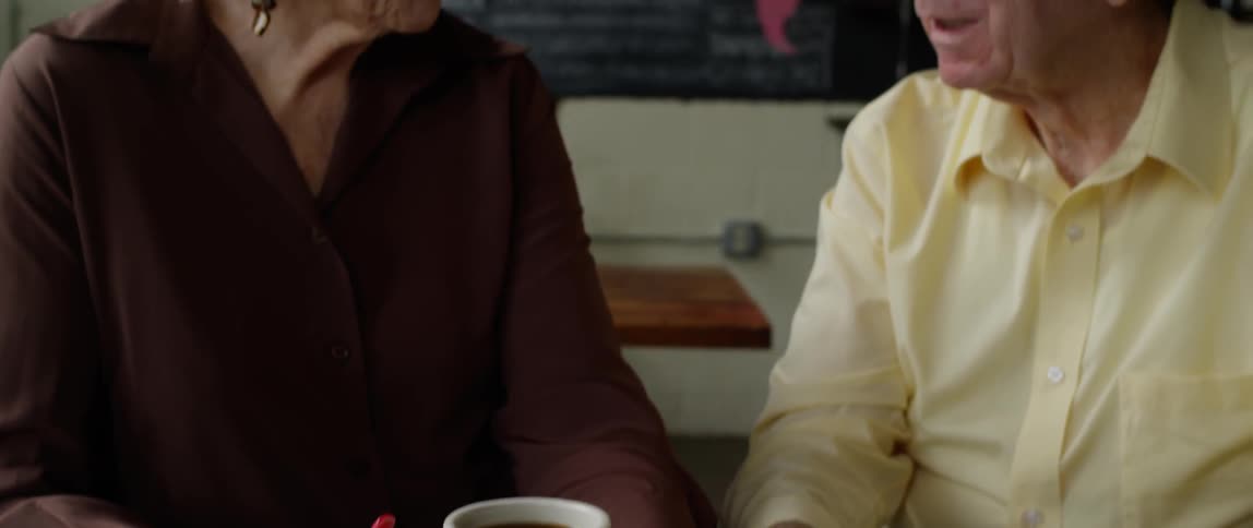 Two people sitting down both holding two full mugs and talking